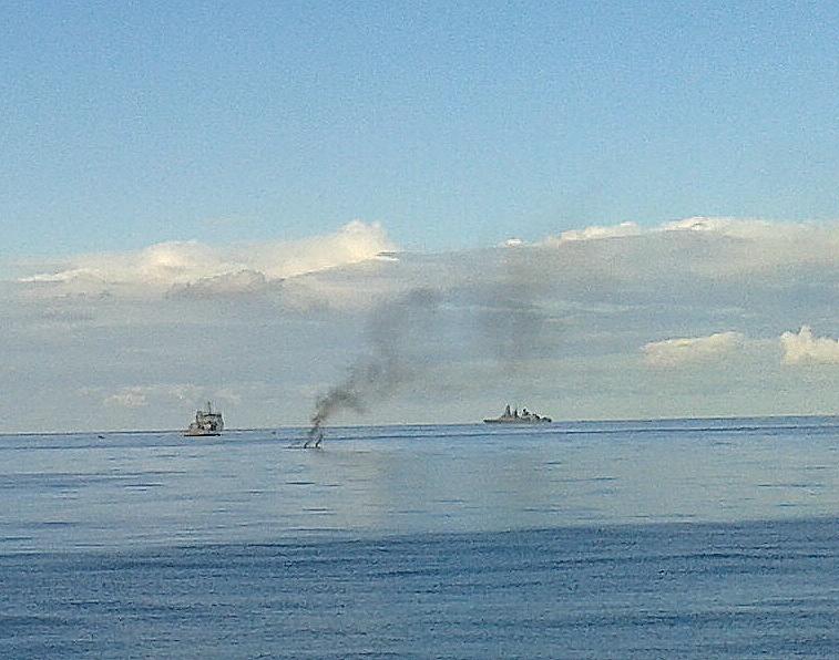 Brennendes Schlauchboot und zwei Kriegsschiffe